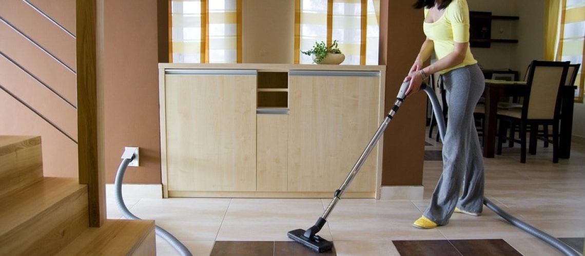 Young woman cleaning floor using a central vacuum system (also known as built-in or ducted vacuum cleaner).